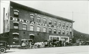 A three story brick building with many arched windows and horse drawn wagons parked in front.